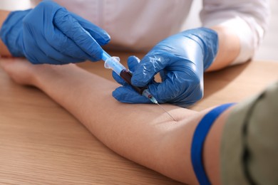 Doctor drawing blood sample of patient with syringe in hospital, closeup