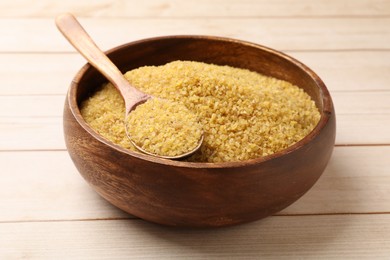 Photo of Bowl and spoon with raw bulgur on light wooden table