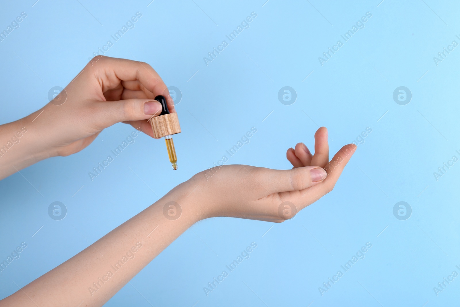 Photo of Woman applying essential oil onto wrist against light blue background, closeup