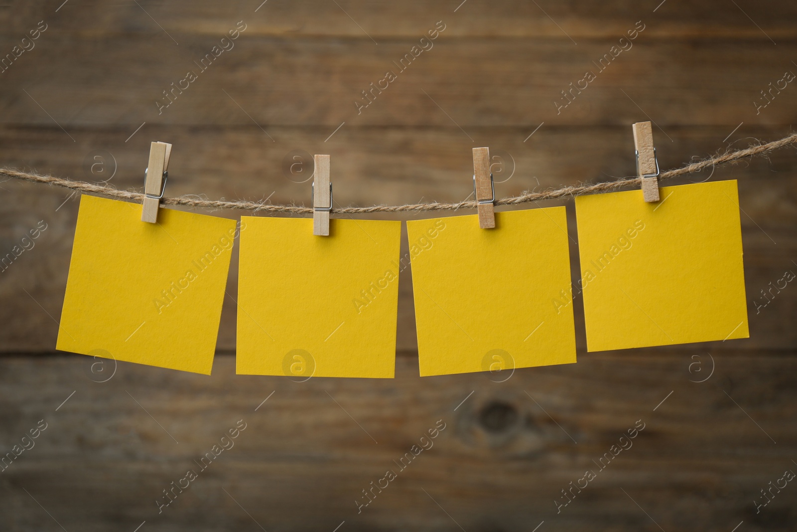Photo of Clothespins with blank notepapers on twine against wooden background. Space for text