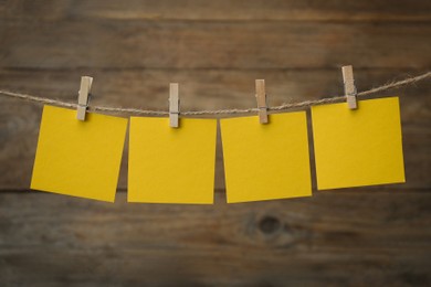 Clothespins with blank notepapers on twine against wooden background. Space for text