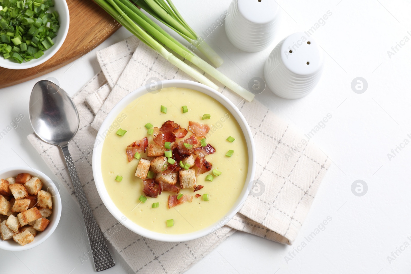 Photo of Tasty potato soup with bacon in bowl served on white table, flat lay