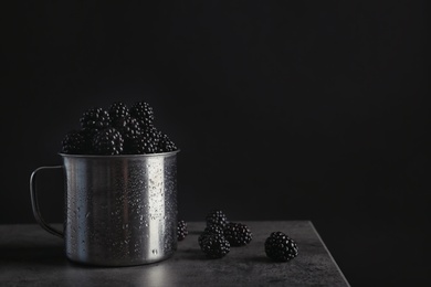 Photo of Mug with fresh blackberry on gray table against dark background. Space for text