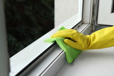 Photo of Woman cleaning window with rag indoors, closeup