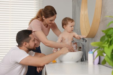 Father and mother washing their little baby in sink at home