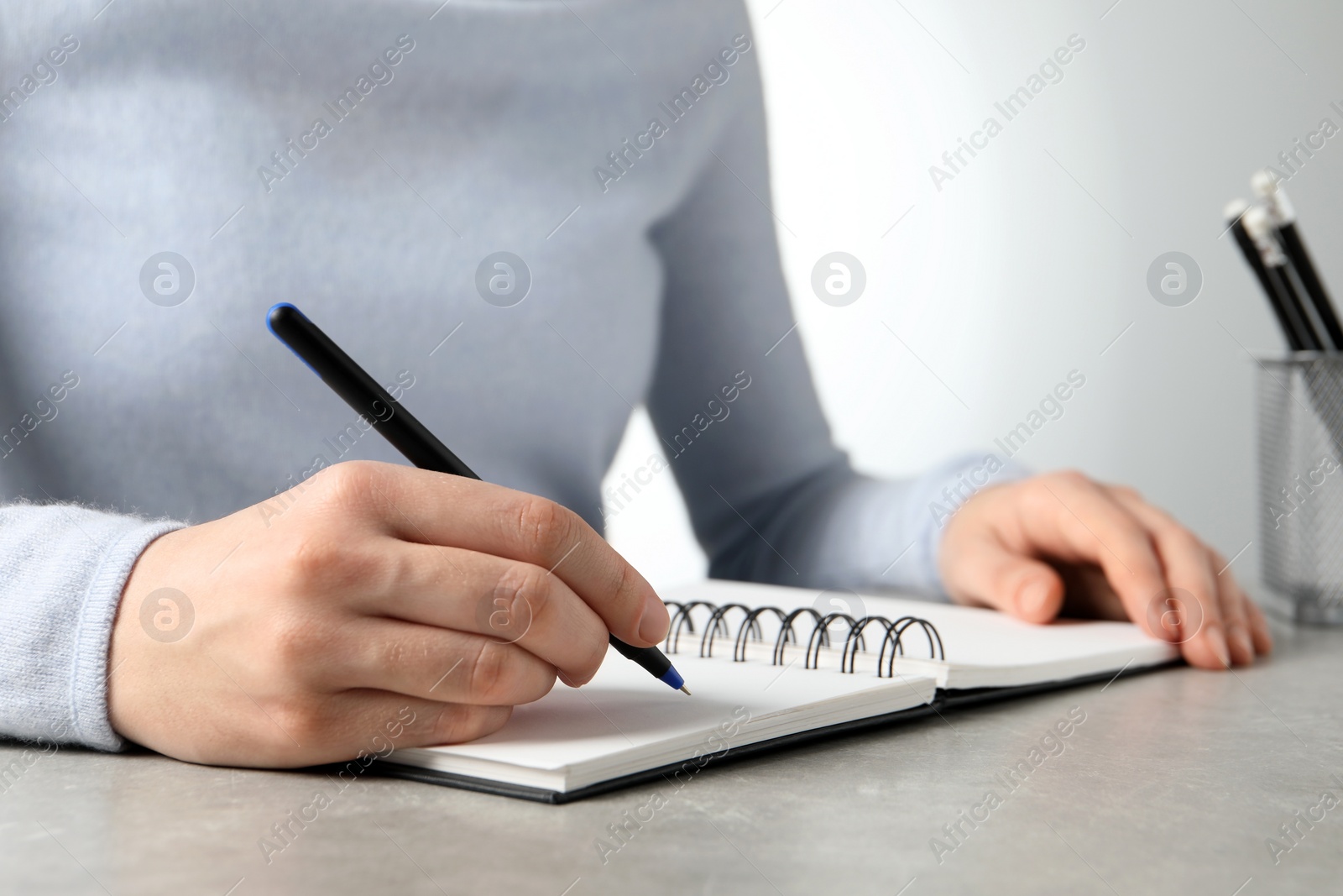 Photo of Woman with pen and notepad at grey table, closeup