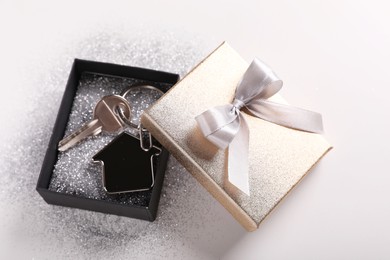 Photo of Key with trinket in shape of house, glitter and gift box on light grey background. Housewarming party