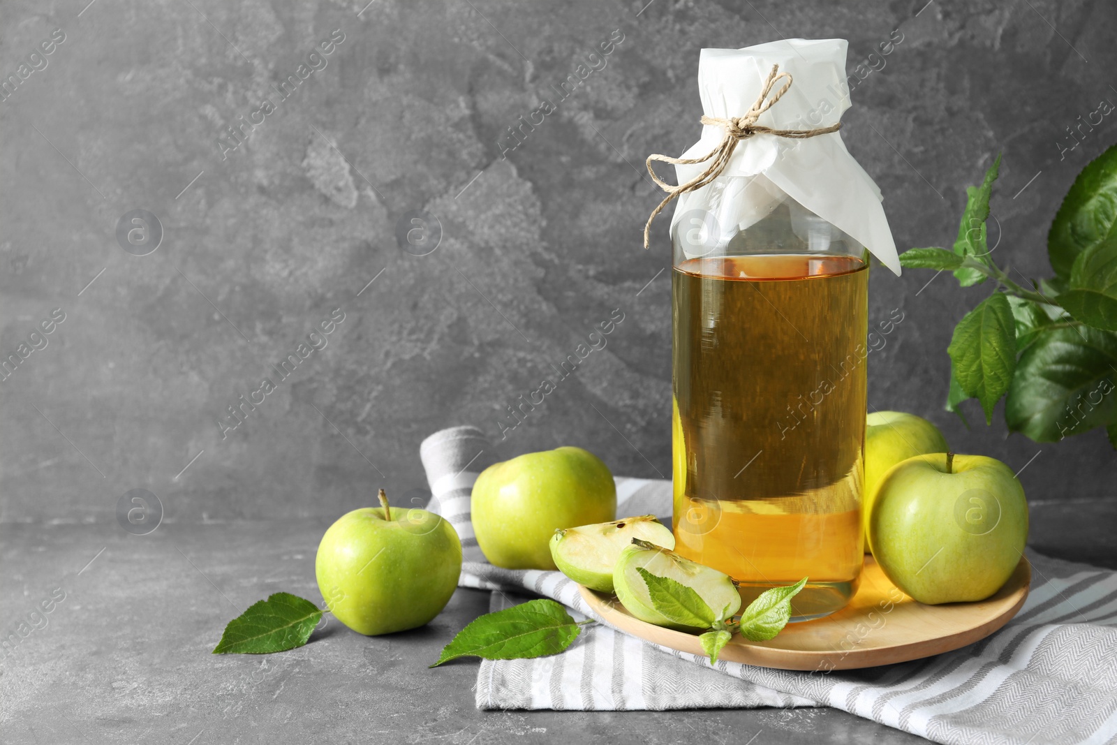 Photo of Delicious cider, ripe apples and green leaves on gray table, space for text