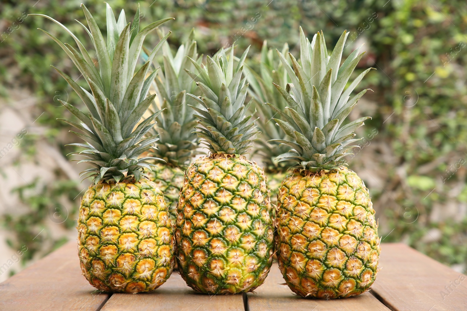 Photo of Delicious ripe pineapples on wooden table outdoors