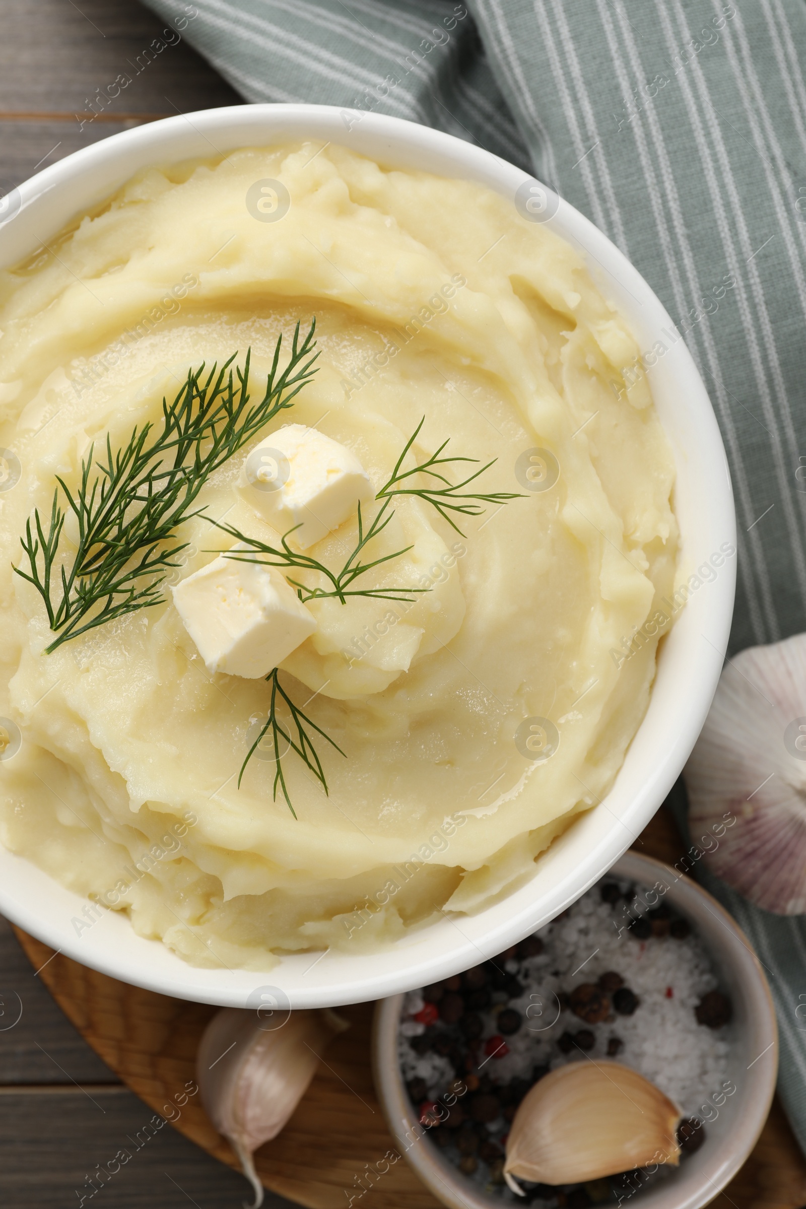 Photo of Bowl of delicious mashed potato with dill and butter on wooden table, flat lay