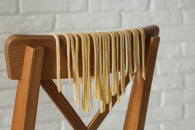 Homemade pasta drying on chair near white wall, closeup