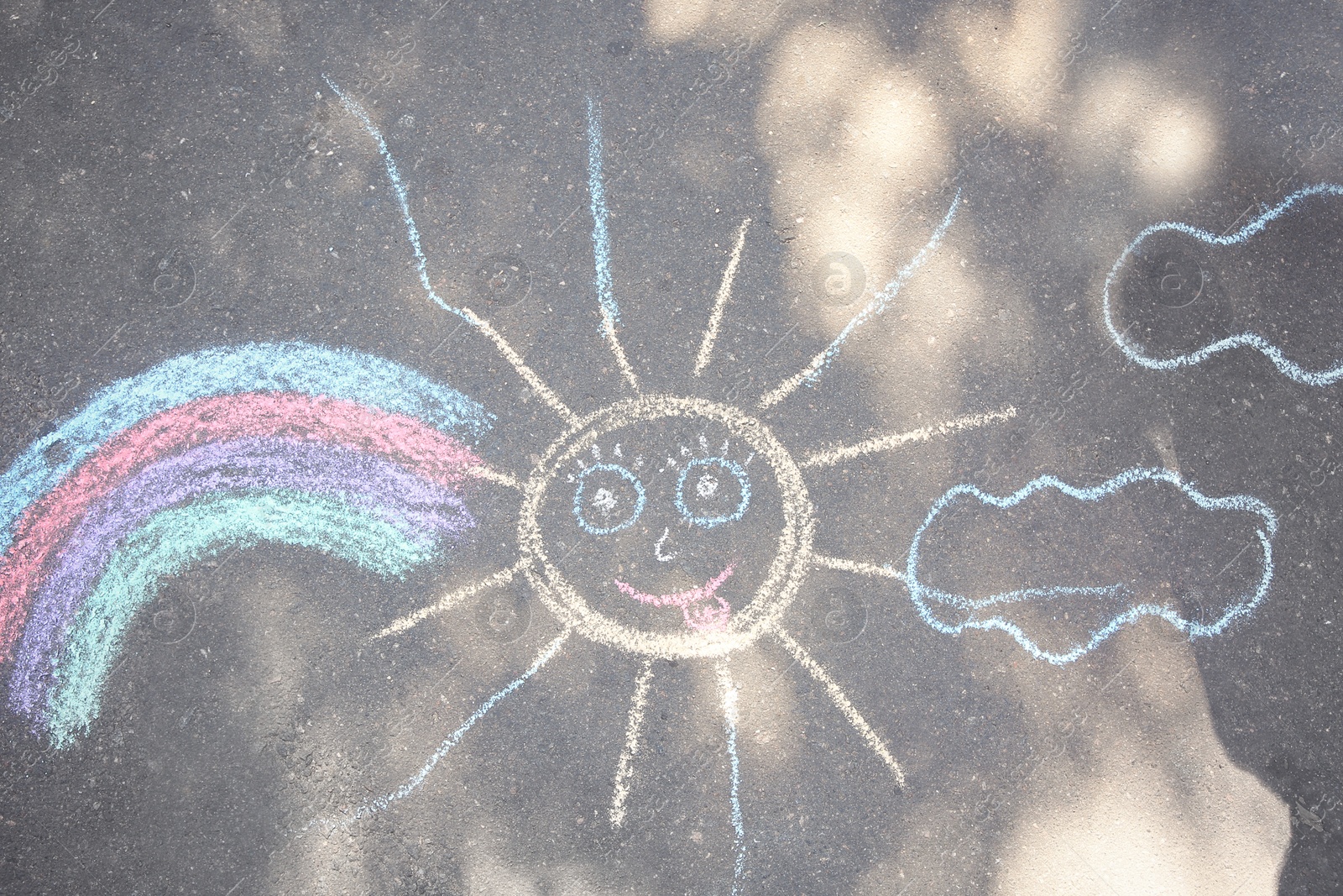 Photo of Child's chalk drawing of sun and rainbow on asphalt, top view