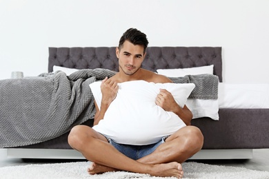 Photo of Sexy young man with soft pillow near bed at home