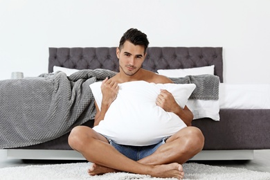 Sexy young man with soft pillow near bed at home