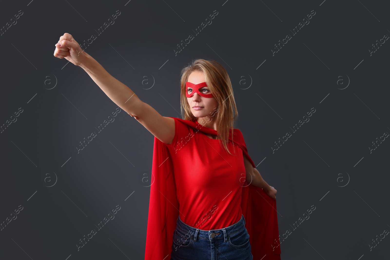 Photo of Confident woman wearing superhero cape and mask on grey background