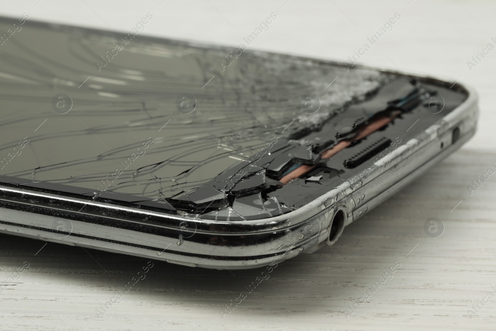 Photo of Smartphone with cracked screen on light beige wooden background, closeup. Device repair