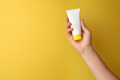 Photo of Woman holding tube of face cream on yellow background, closeup. Space for text