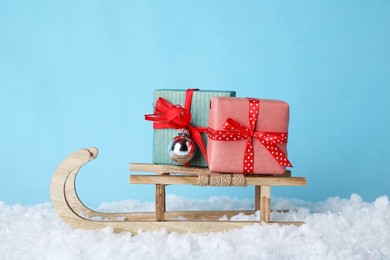 Photo of Wooden sleigh with gift boxes, Christmas bauble and artificial snow on light blue background