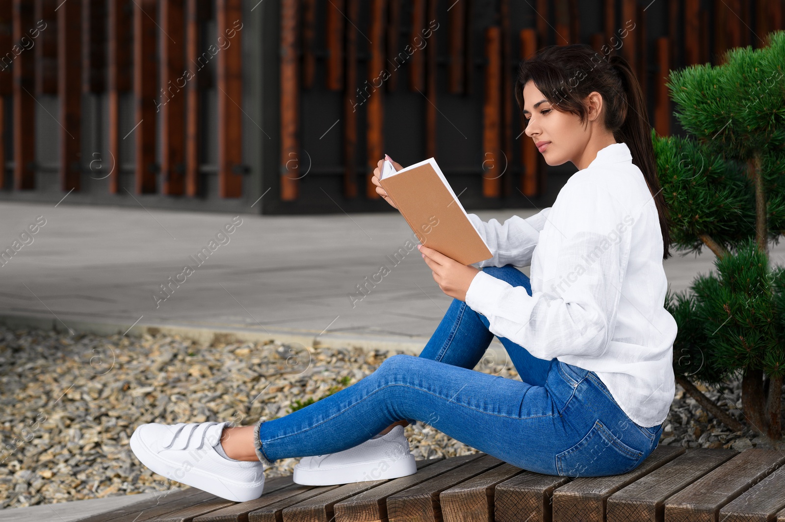 Photo of Young woman reading book on bench outdoors