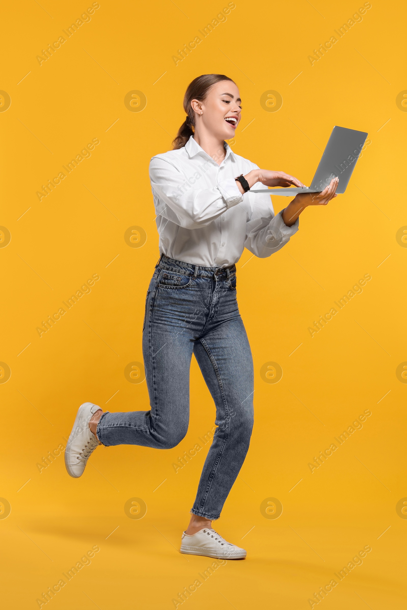 Photo of Happy woman with laptop running on orange background