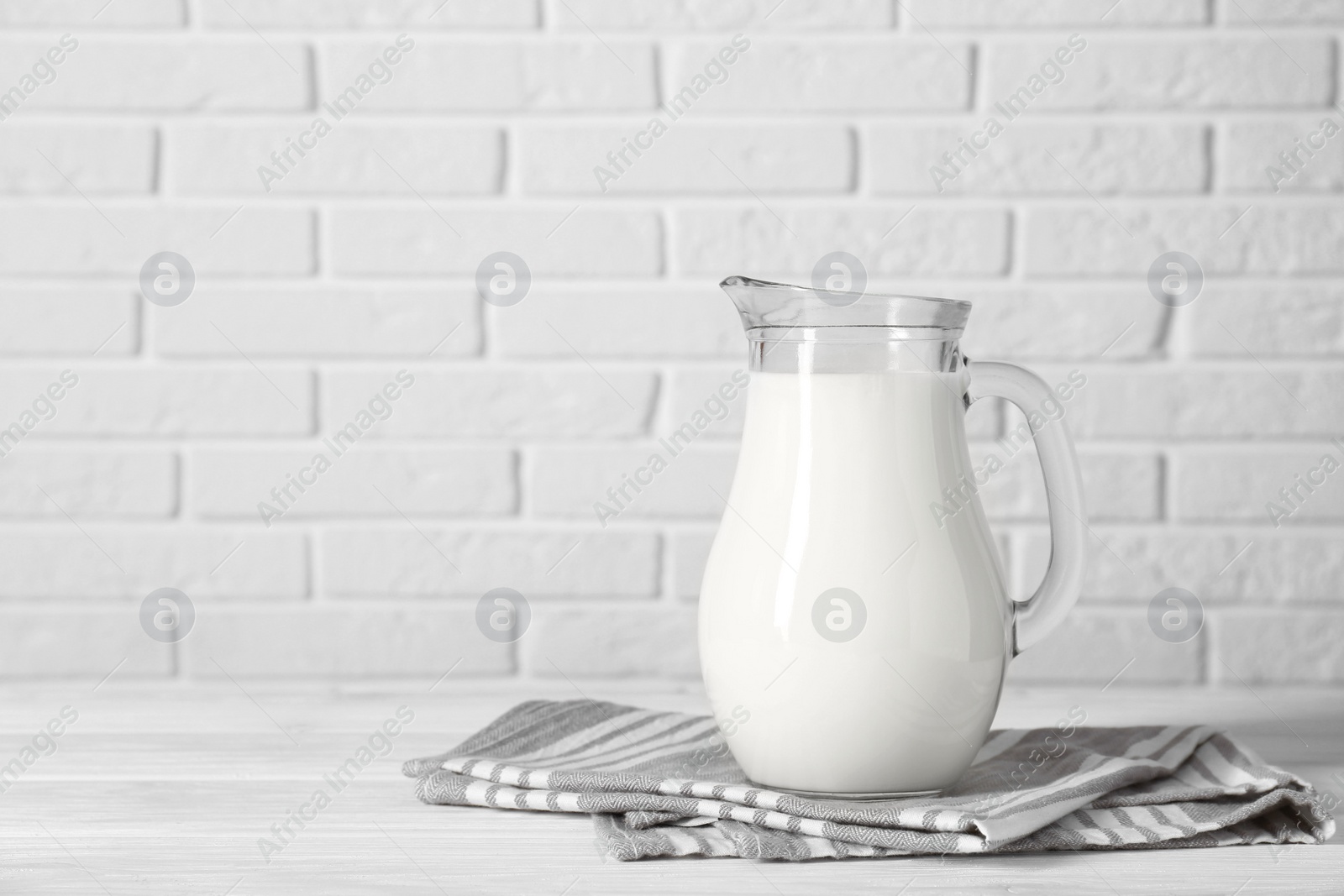 Photo of Jug of fresh milk on white wooden table, space for text