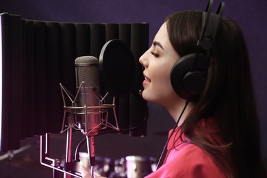 Young singer with microphone recording song in studio