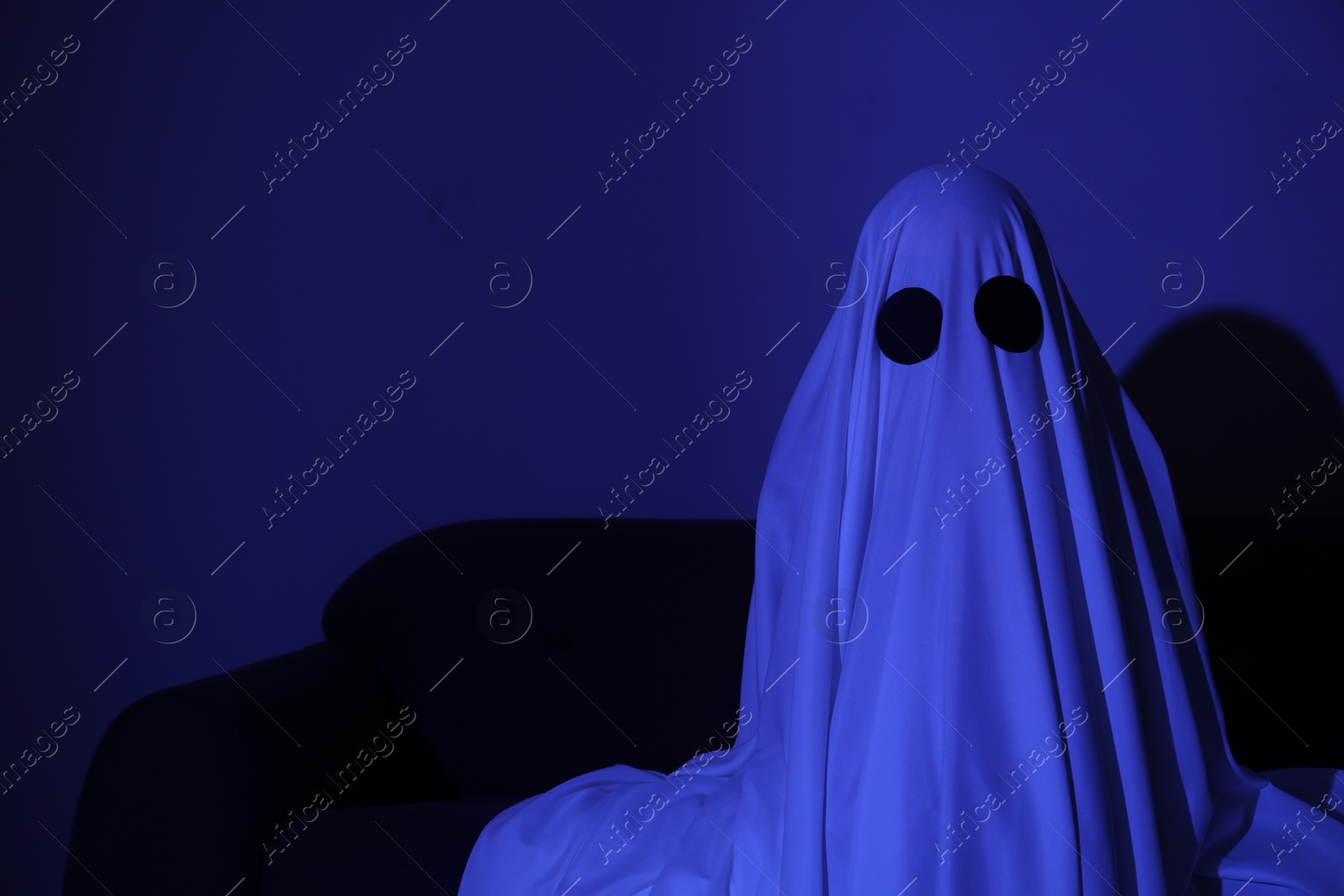 Photo of Creepy ghost. Woman covered with sheet in blue light, space for text