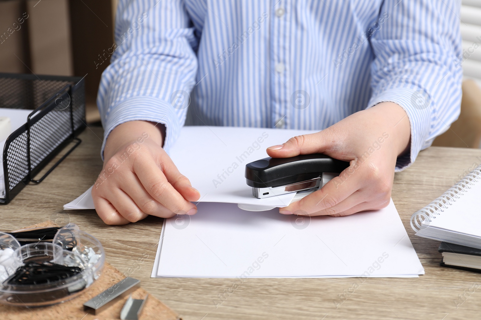 Photo of Woman with papers using stapler at wooden table indoors, closeup