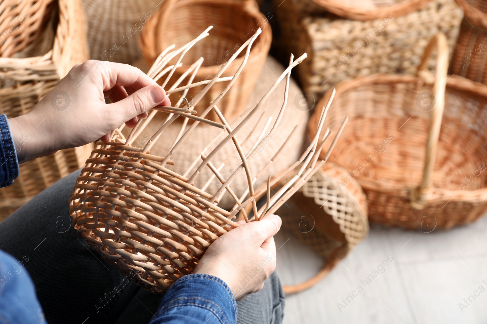 Photo of Woman weaving wicker basket indoors, closeup view