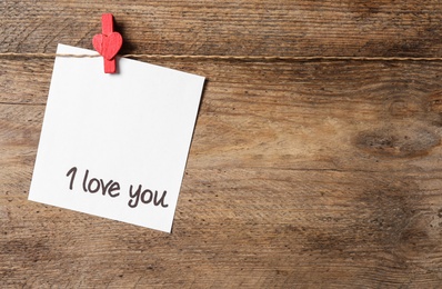 Card with words I Love You hanging on wooden background. Space for text