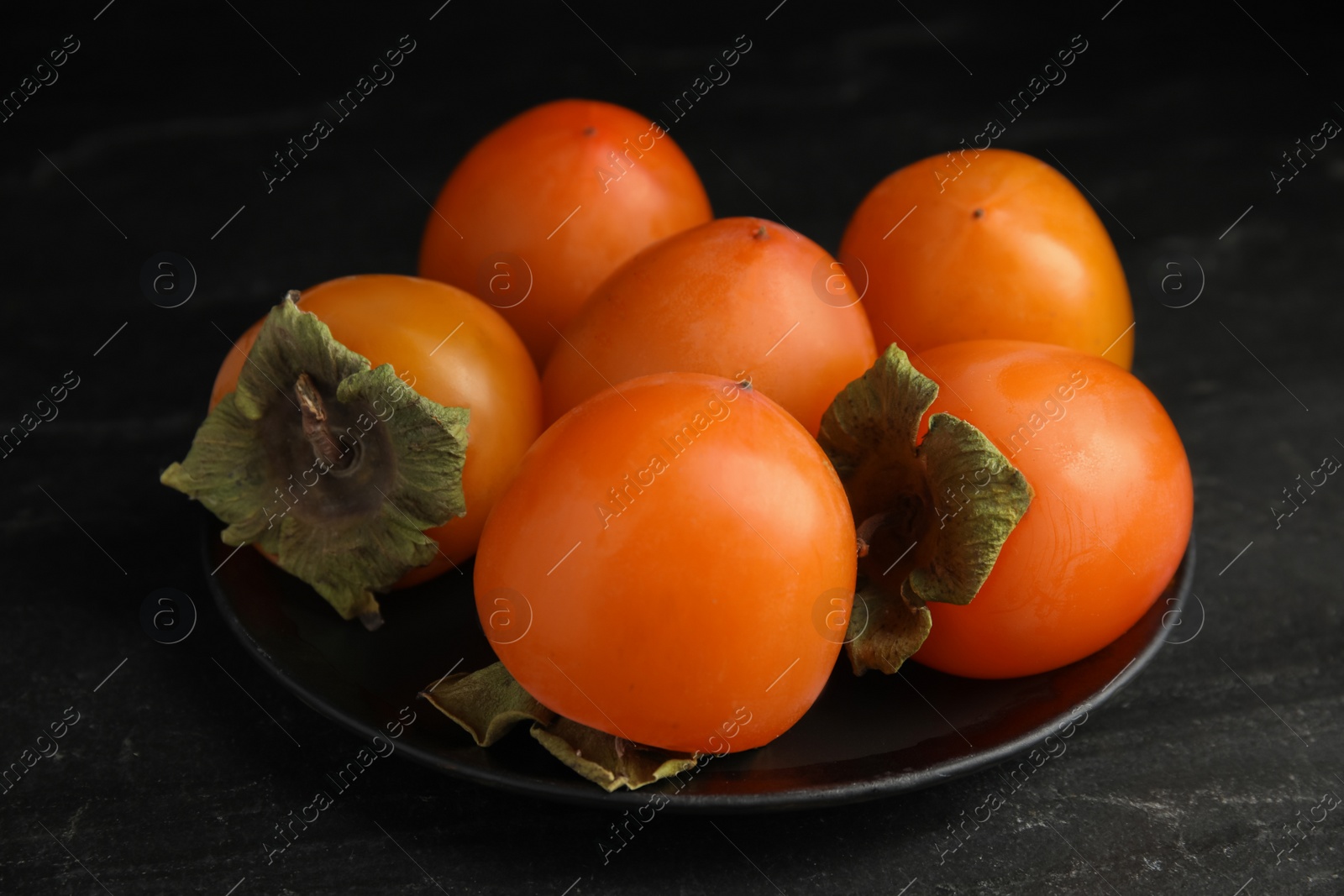 Photo of Tasty ripe persimmons on black slate table, closeup