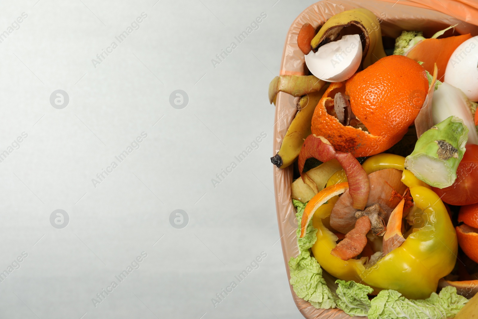 Photo of Natural garbage in trash bin on light background, top view with space for text. Composting of organic waste