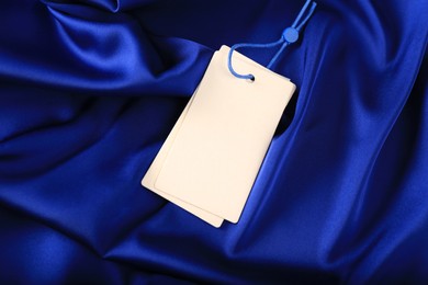Photo of Blank white tags on blue silky fabric, top view. Space for text