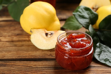 Photo of Delicious quince jam and fruit on wooden table, closeup