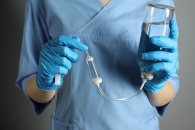 Nurse with IV infusion set on grey background, closeup