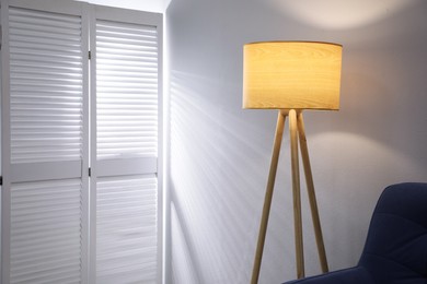 Stylish tripod floor lamp near blue armchair indoors, space for text. Interior design