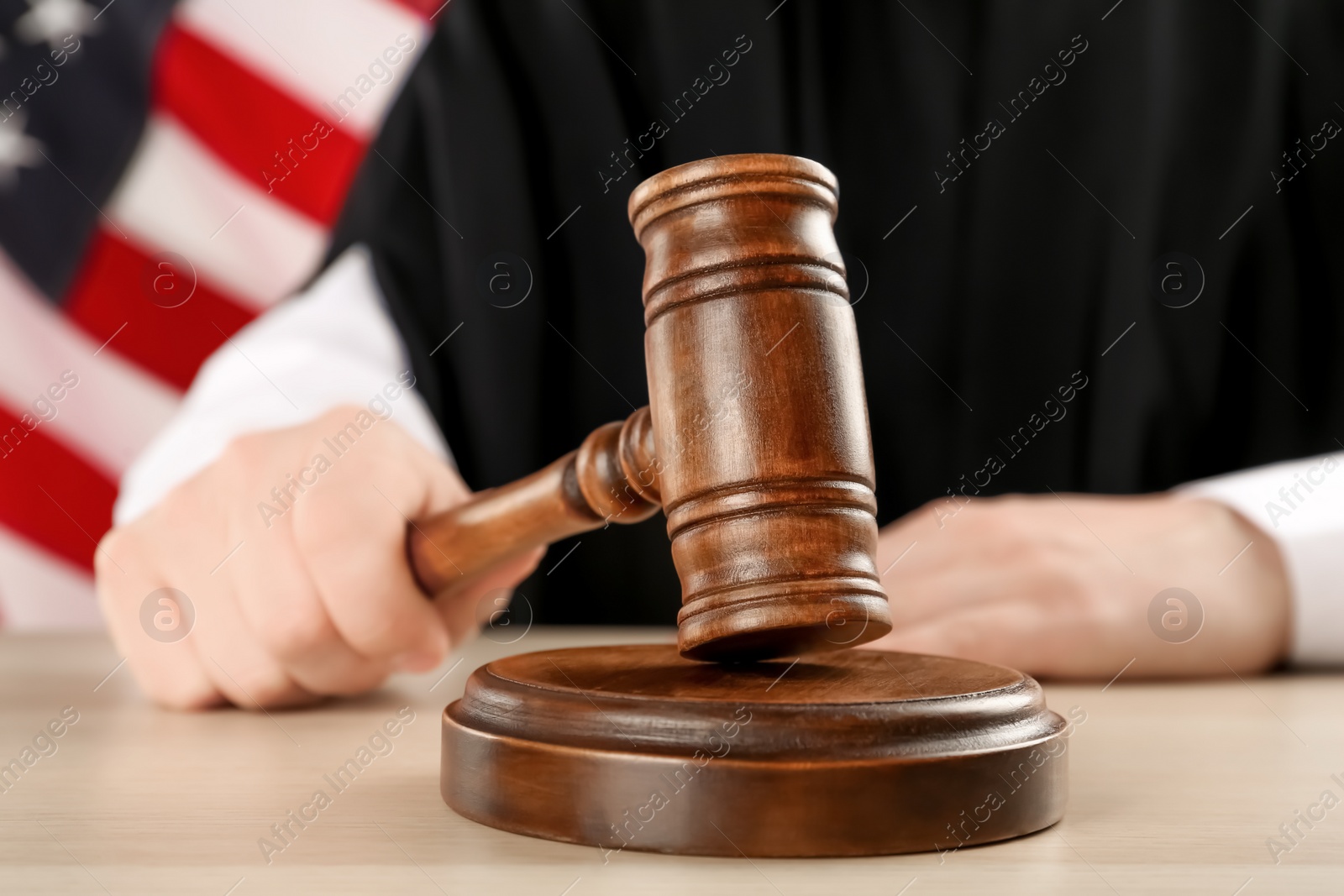 Photo of Judge with gavel at light wooden table near American flag, closeup