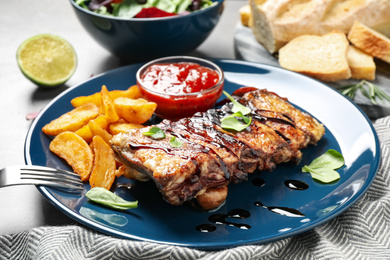 Delicious grilled ribs with potato and sauce on table, closeup