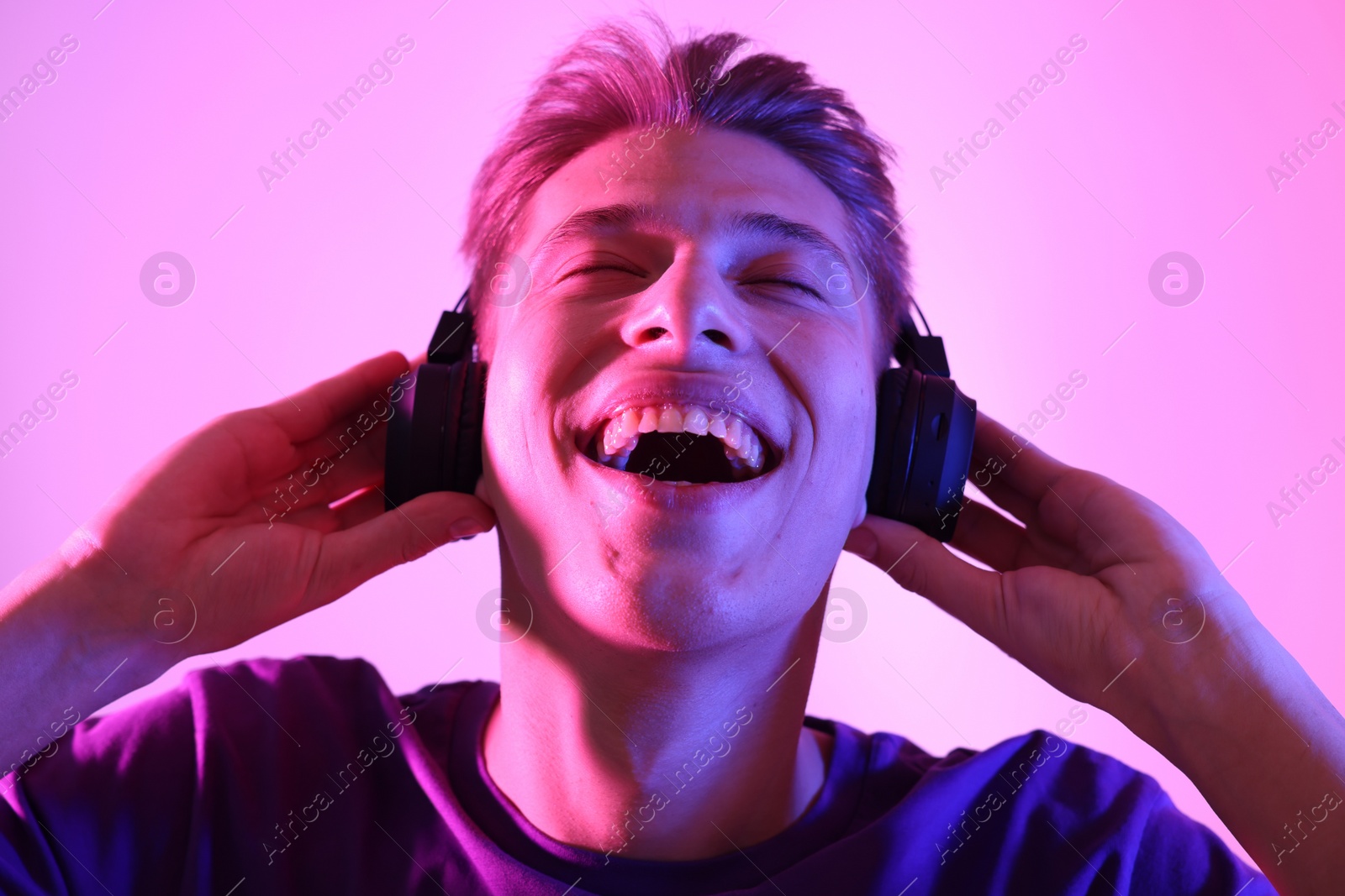 Photo of Young man with headphones on pink background in neon lights