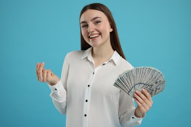 Happy woman with dollar banknotes showing money gesture on light blue background