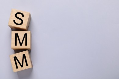 Photo of Wooden cubes with abbreviation SMM (Social media marketing) on grey background, flat lay. Space for text