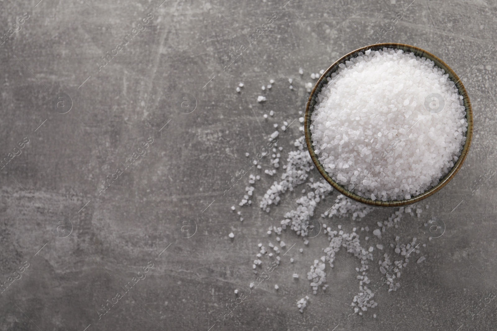 Photo of Bowl of natural sea salt on grey table, top view. Space for text