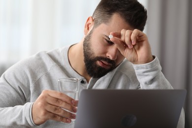 Photo of Young man taking pill against headache in office