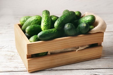 Photo of Crate full of fresh ripe cucumbers on white wooden table