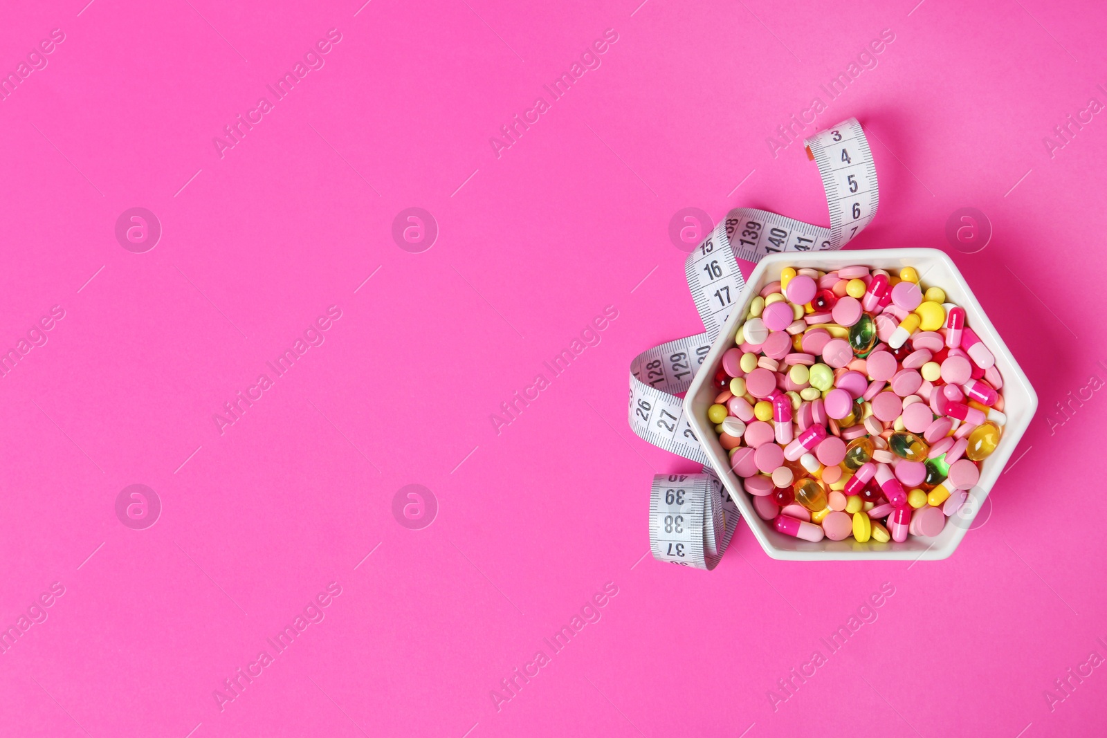 Photo of Bowl with weight loss pills and measuring tape on color background, top view. Space for text