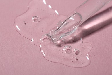 Dripping cosmetic serum from pipette onto pink background, macro view