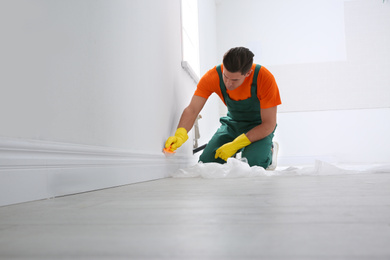 Photo of Professional janitor cleaning baseboard with brush after renovation indoors