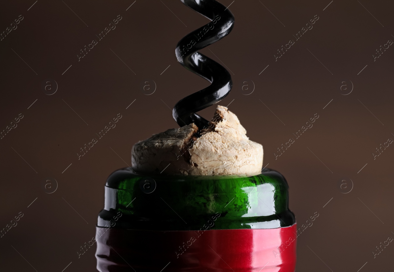 Photo of Opening wine bottle with corkscrew on dark background, closeup