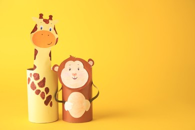 Photo of Toy monkey and giraffe made from toilet paper hubs on yellow background, space for text. Children's handmade ideas