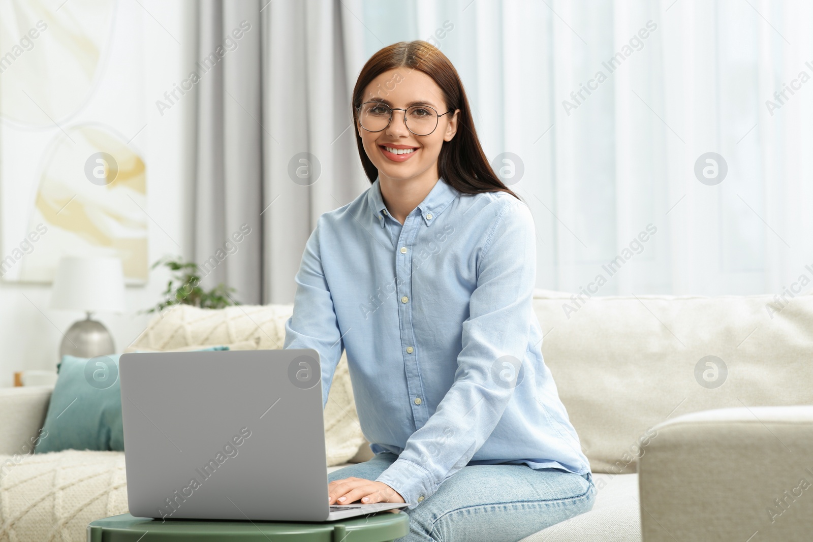 Photo of Portrait of smiling woman in stylish eyeglasses near laptop at home